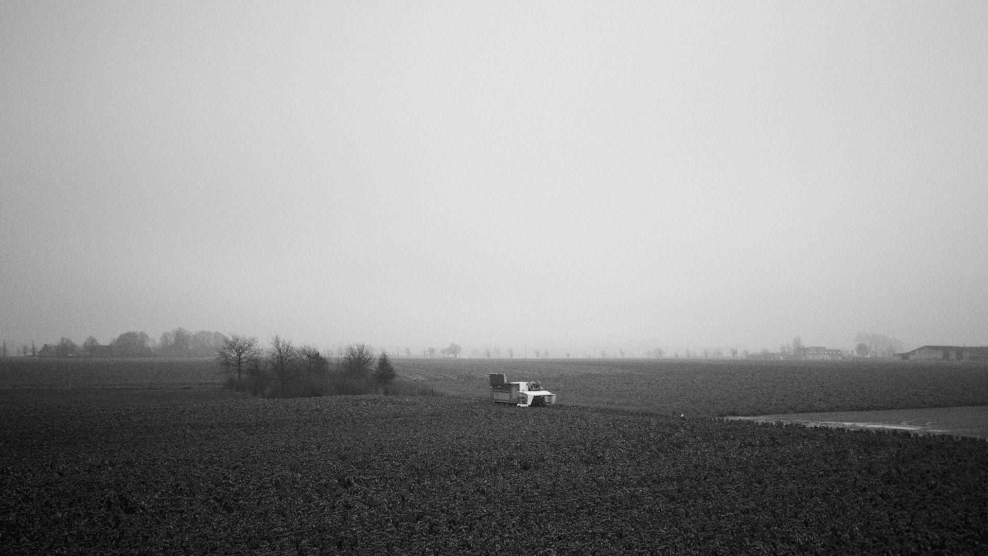 Image en noir et blanc d'une machine agricole dans la campagne, avec des fermes en arrière-plan